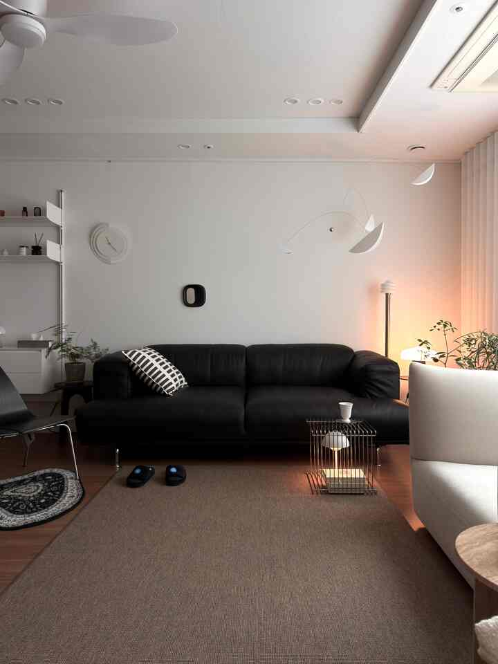 モダンな黒いソファを中心に据えたリビング、白い壁とブラウンのラグが調和した雰囲気のある空間
