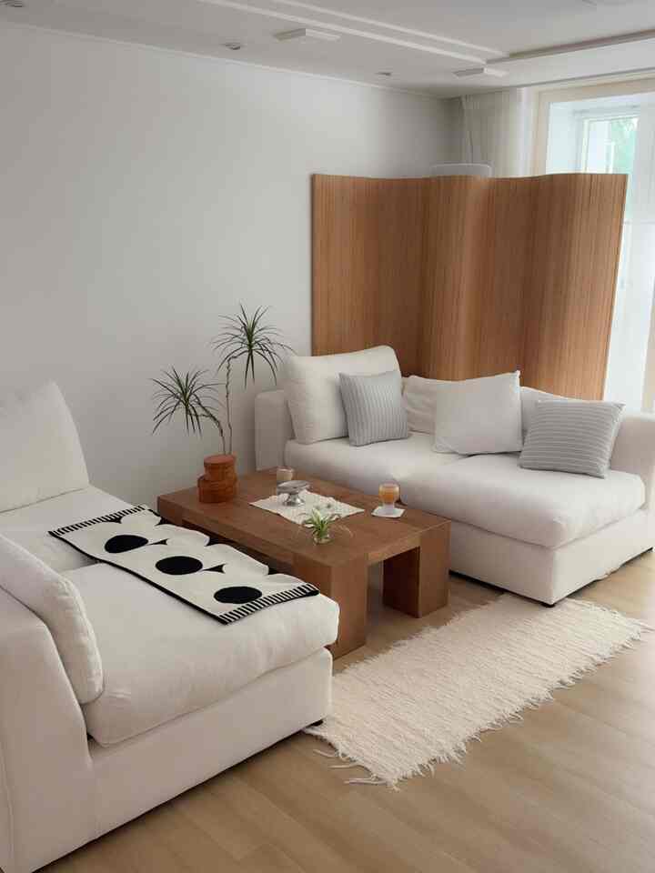 ナチュラルな色調のリビング、白いソファと木製の間仕切り、木製コーヒーテーブル、ラグが配置された落ち着いた空間