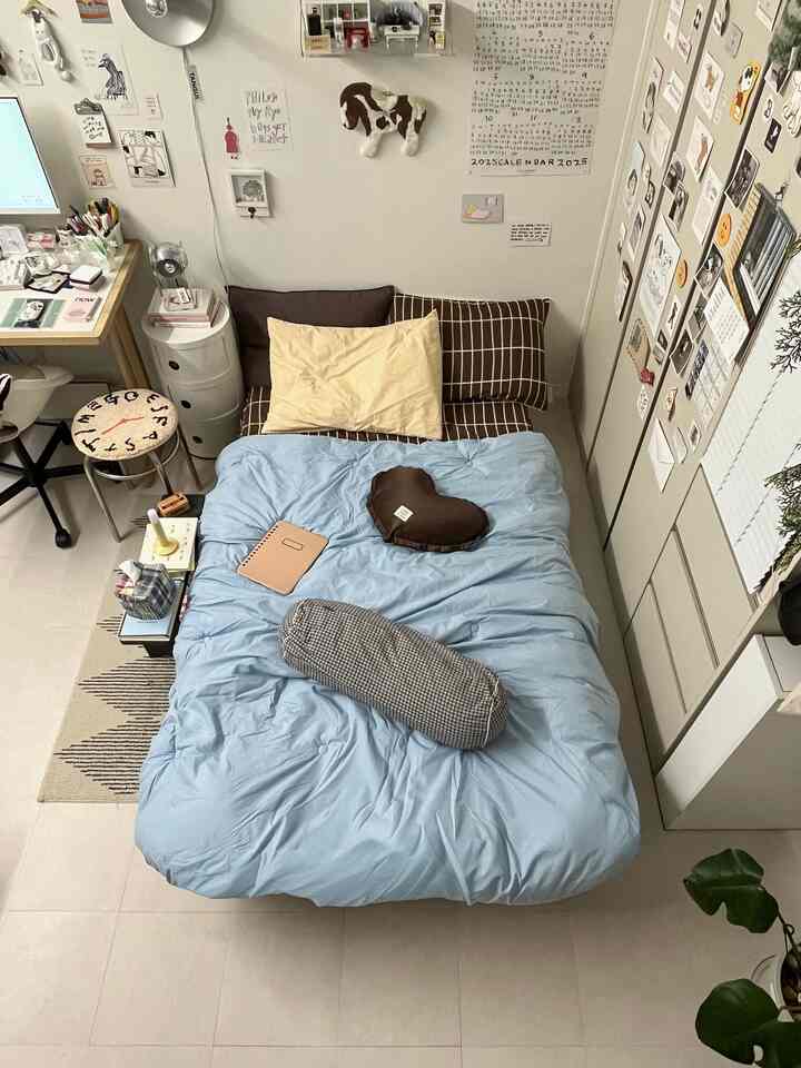 淡いブルーの寝具が置かれた小さな寝室で、右壁にビルトインクローゼットがあり、机とラグが配置された雰囲気のある空間