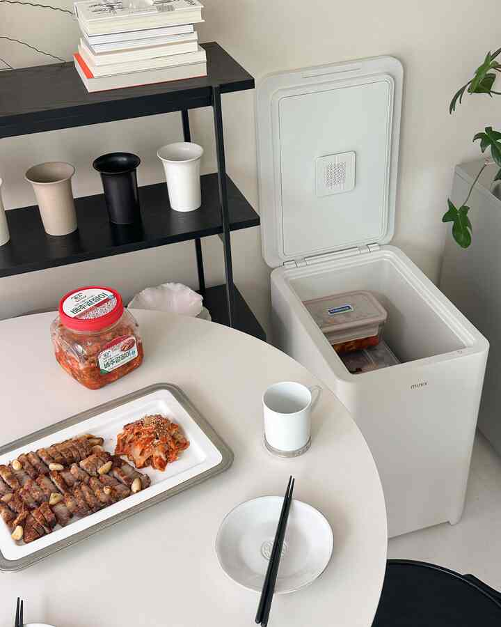 白を基調としたキッチン空間、丸いダイニングテーブルと黒の棚、開いたミニ冷蔵庫が配置された清潔感のあるインテリア