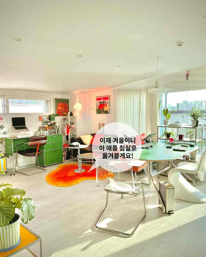 明るいグリーンとオレンジのアクセントがあるダイニング兼ホームオフィス、透明な椅子と植物が配置された自然な雰囲気のインテリア