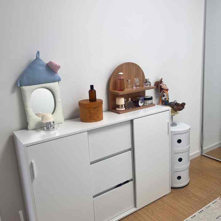 白い壁とキャビネットのあるウォークインクローゼット、丸い収納と木目調の小物が配置された清潔感のある空間