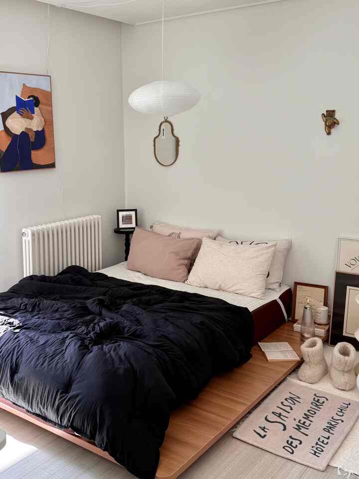 白い壁と茶色の木目調の低いベッドがあるモダンな寝室、中央に楕円形のペーパーランプが吊り下げられた居心地の良い空間