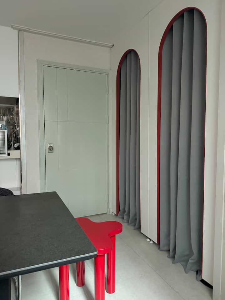 赤い家具とグレーのカーテンが配置されたモダンでミニマルな狭い玄関空間