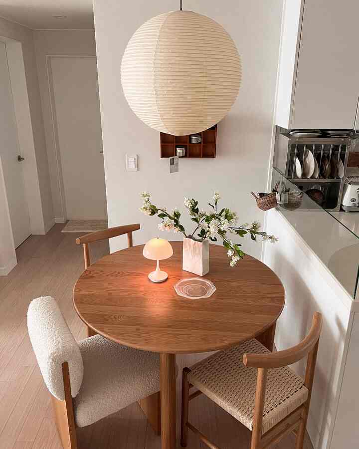 ナチュラルな木目調のキッチンダイニング、丸い木製ダイニングテーブルと様々な素材の椅子が配置されたシンプルで温かみのある空間