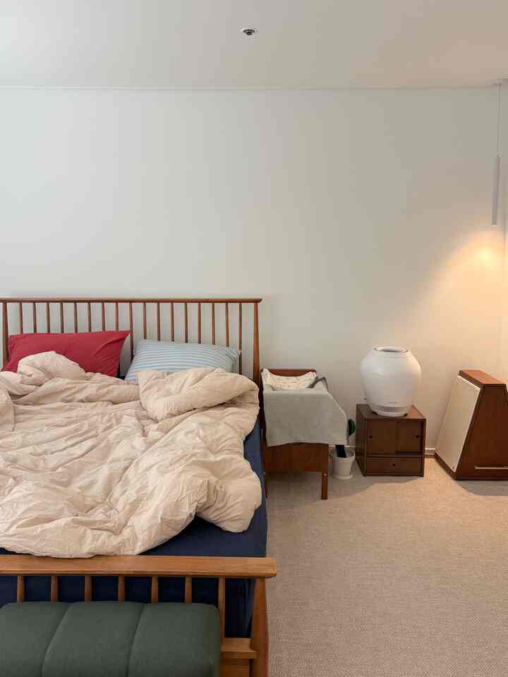 ナチュラルトーンの木製ベッドとベージュの寝具が置かれた落ち着いた寝室、ホワイトの壁と暖かい照明が調和している