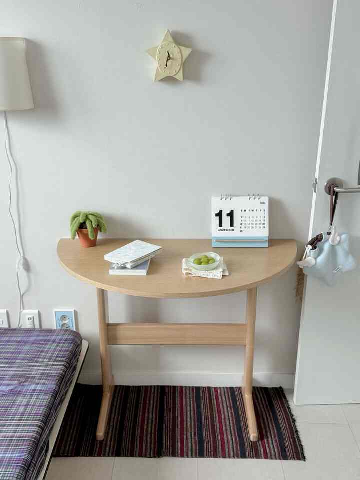 ナチュラルトーンのワンルーム小部屋に配置された半円形の木製テーブルとシンプルな小物が印象的な空間