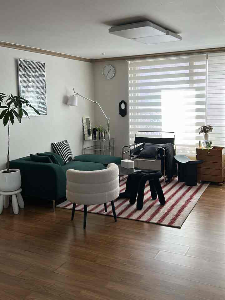 ナチュラルな木目調の床と白いカーテンが調和するモダンなリビング、緑のソファと黒いスツールが配置された落ち着きのある空間