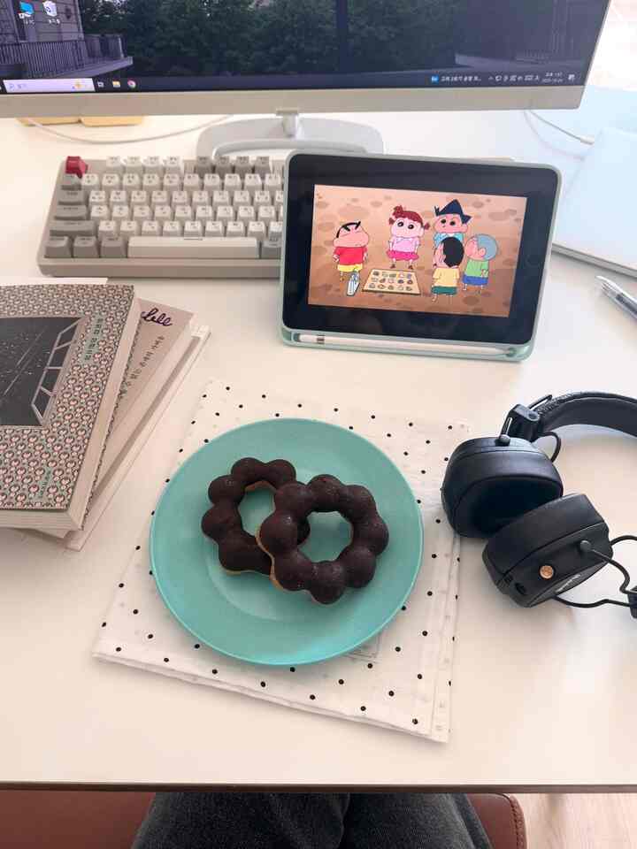 白を基調としたホームオフィス空間、机上にキーボード、ヘッドホン、タブレット、チョコレートドーナツの皿が置かれた整った作業スペース