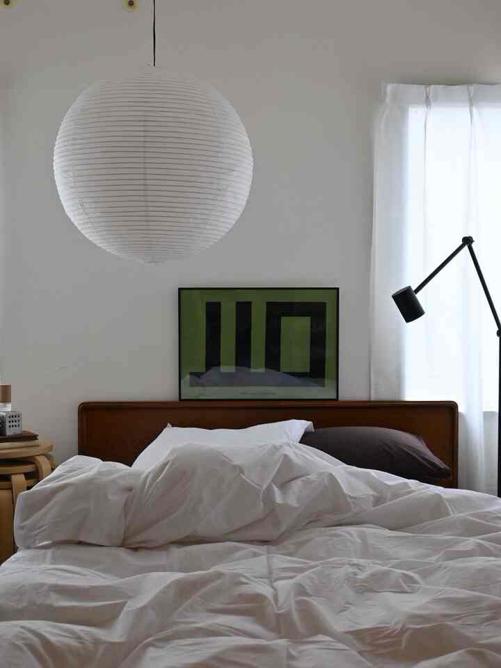 白を基調とした寝室、ミッドセンチュリーモダンの木製ベッドとペンダントライトが配置された、落ち着いた自然な雰囲気のインテリア