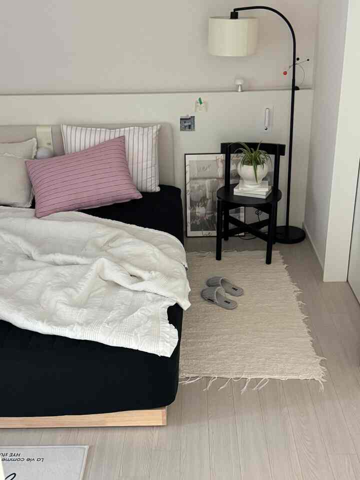 明るい床と壁に黒の低めベッドフレームと白い寝具が配置されたシンプルな寝室のインテリア