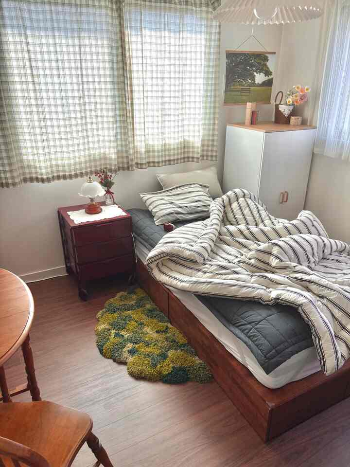 ナチュラルモダンの6畳寝室、木目調のベッドフレームとストライプの寝具、チェックのカーテンが配置された落ち着いた空間