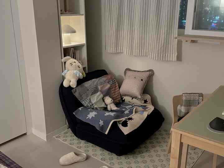 ナチュラルな色調のコンパクトなワンルーム、黒のソファと木製のデスク、白い本棚が配置されたシンプルな空間