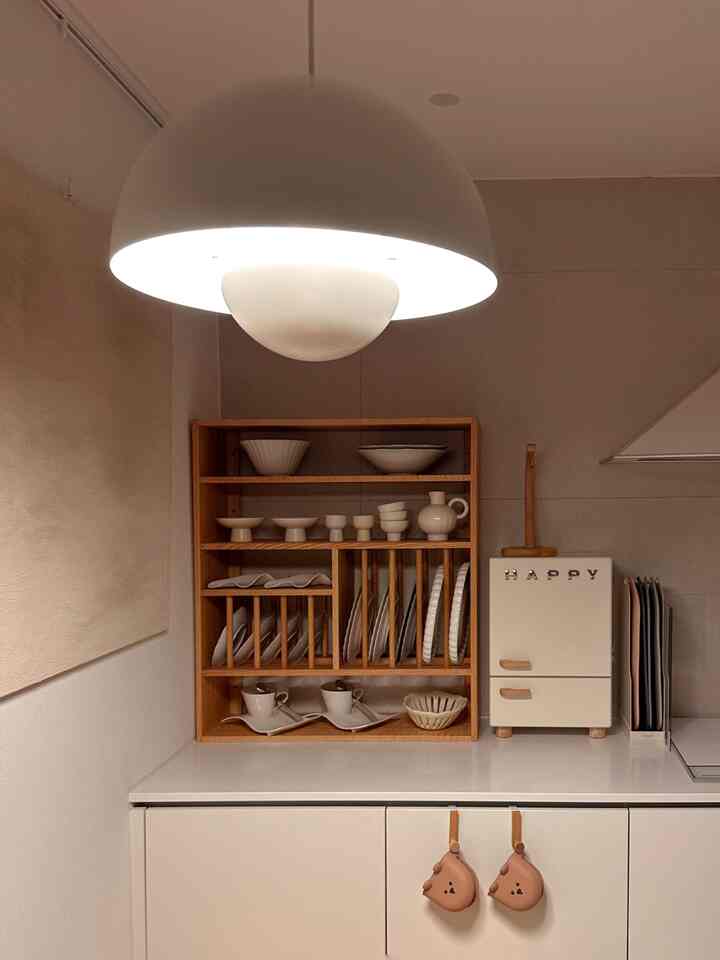 白と茶色のトーンのキッチン空間、木製のプレートラックとペンダントライトが配置された雰囲気のあるインテリア