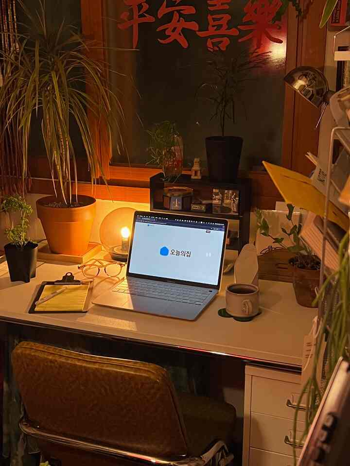 暖かみのあるブラウンとホワイトトーンのホームオフィス空間、植物とノートパソコンが置かれた整ったデスクとヴィンテージチェアが配置された雰囲気のある部屋