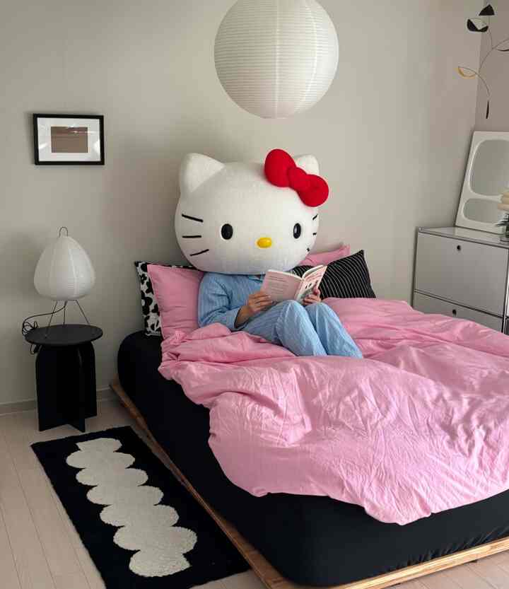 ピンクと黒の調和が美しい寝室、大きなハローキティの頭部のオブジェとシンプルな家具が配置された雰囲気のあるインテリア