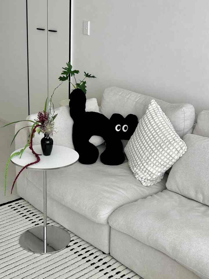 白と黒の色調のリビング、明るいソファに猫形のクッション、丸いサイドテーブルとラグが配置されたモダンな空間