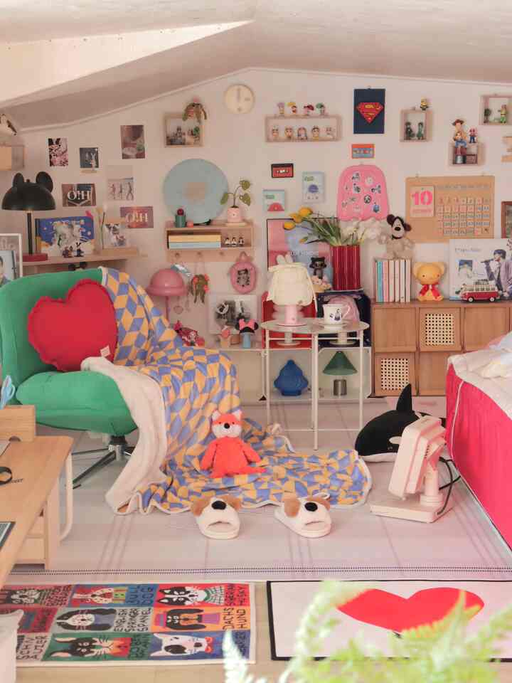 明るくかわいらしいトーンの小さな部屋、グリーンの椅子と赤いクッション、多彩な玩具や小物が配置された雰囲気のある空間