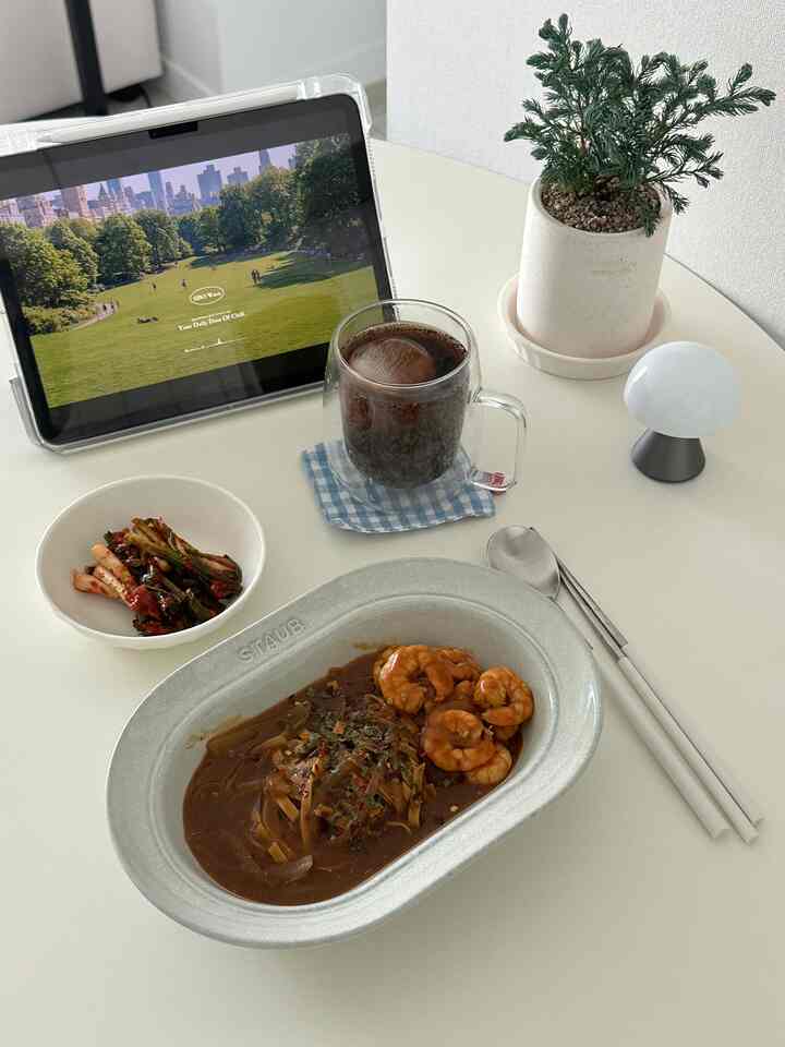 白の丸いダイニングテーブルに、カレー入りのストウブ皿と副菜、アイスドリンクのグラス、植物、タブレットが整然と配置された食事スペース