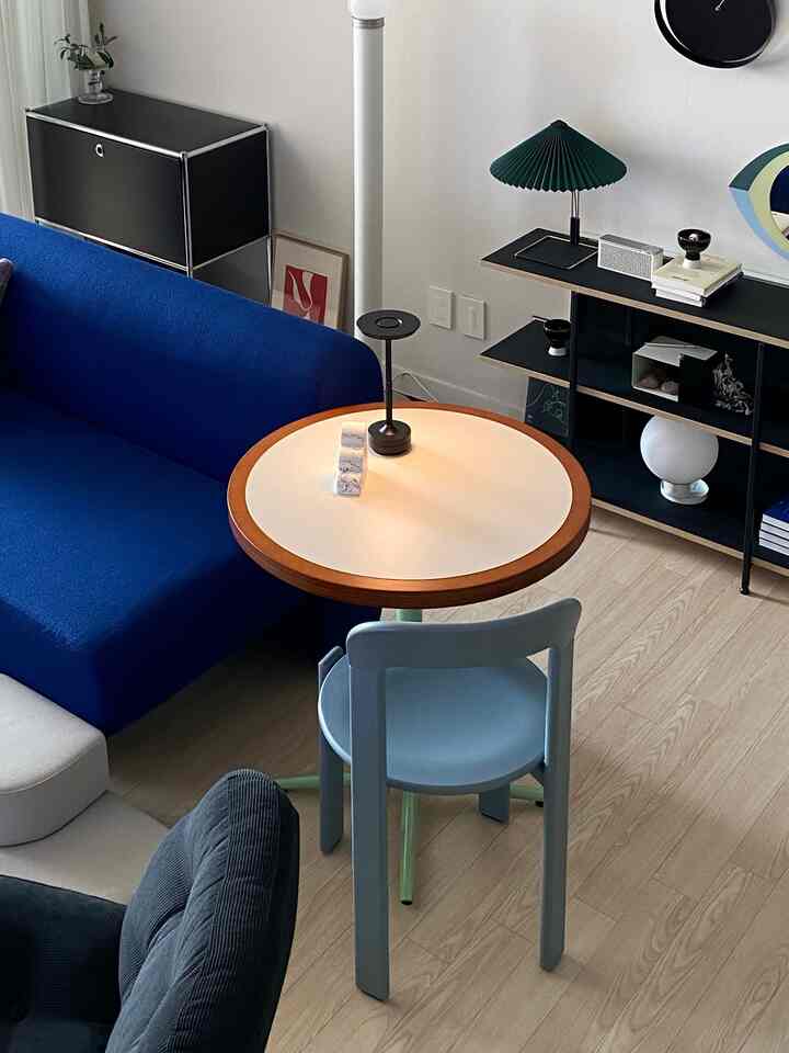Modern living room with white walls and wood-tone flooring, featuring a blue sofa, round coffee table, black storage cabinet, and green table lamp