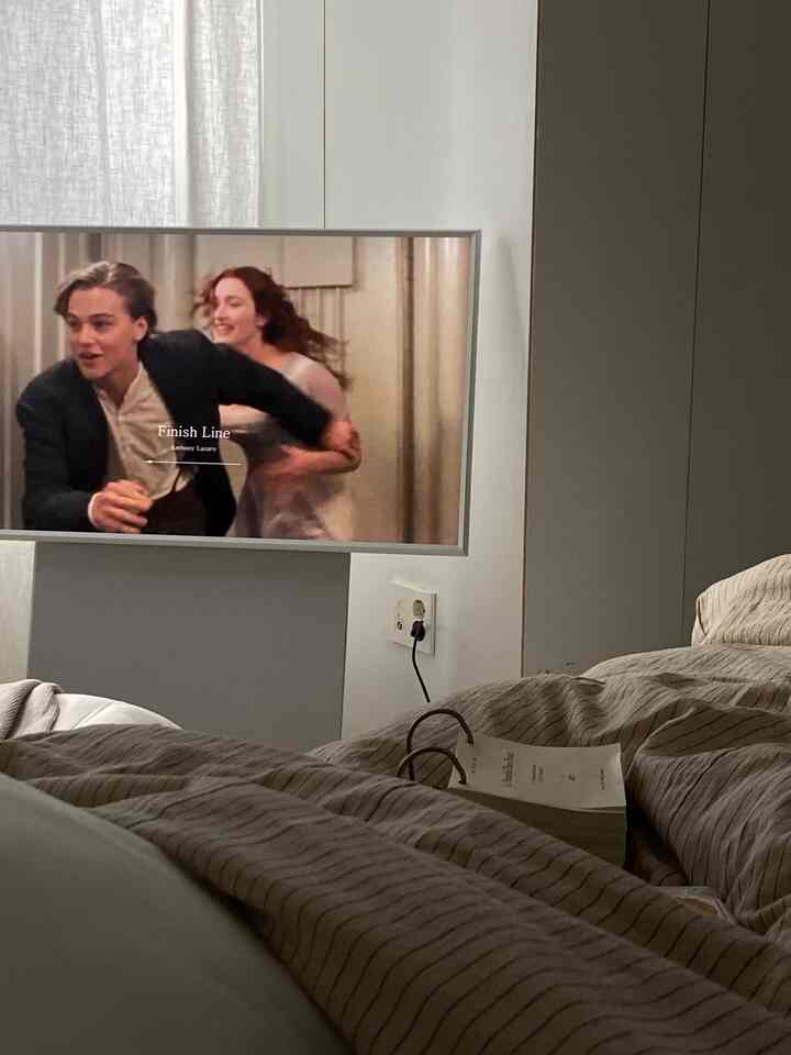 ベージュと白のトーンの6畳寝室、ベッドフレームとテレビ台が配置されたモダンな空間