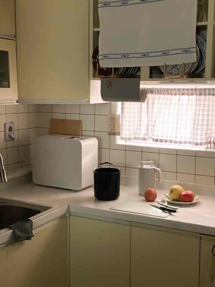 ナチュラルカラーと木目調が調和するコンパクトなキッチン、カーテンのある窓と調理器具が配置された雰囲気のあるインテリア