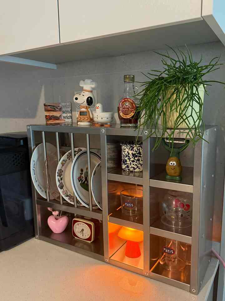 白とシルバーのトーンのキッチン空間、ステンレス収納ラックに皿や小さな調理器具が整頓されたモダンなインテリア