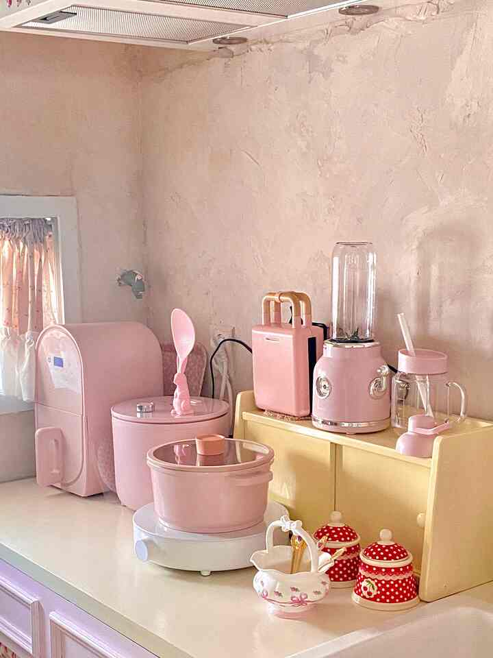 淡いピンクとバター色調のキッチン、ピンクの家電とミニ木製収納が配置された温かみのあるヴィンテージ風インテリア