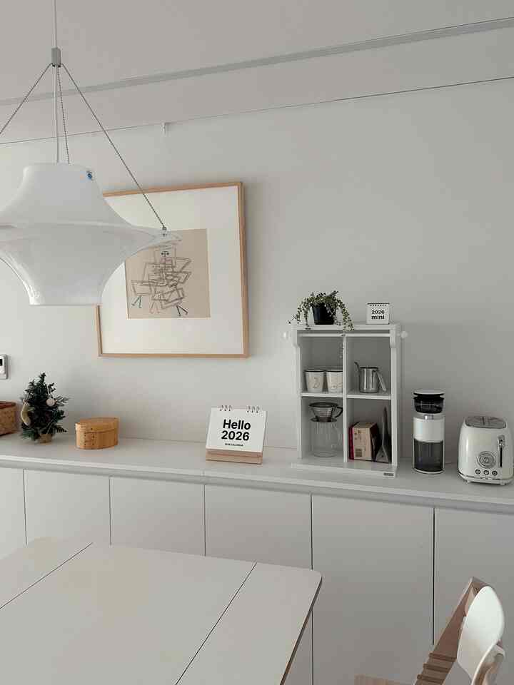 白とナチュラルウッドのキッチン空間、シンプルでモダンな卓上カレンダーとコーヒー用品が配置された清潔感のあるインテリア