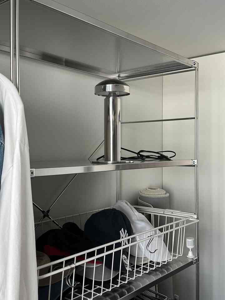 シルバー調のウォークインクローゼットの金属棚にステンレス製のテーブルランプが置かれたシンプルでモダンなインテリア