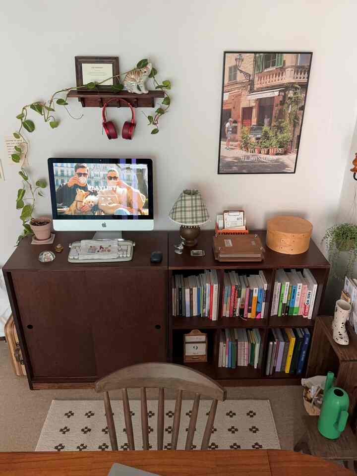 ナチュラルな色調の書斎、木製の本棚とデスク、ポスターと植物が配置された温かみのあるインテリア