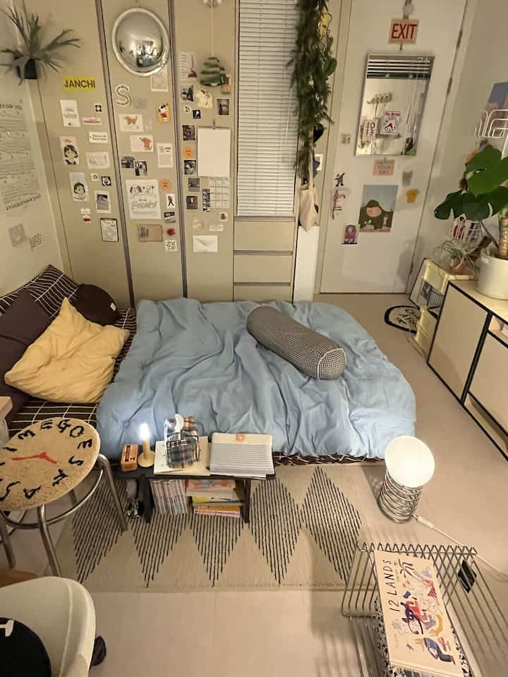 Small single bedroom in beige and brown tones featuring a cozy bed and a multifunctional shelf table