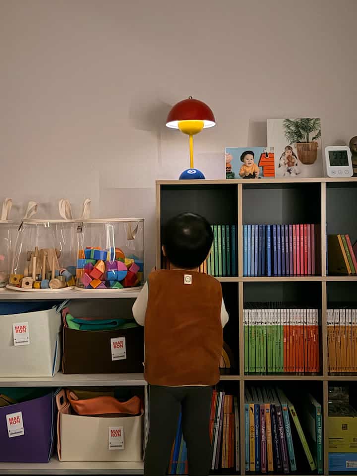 白と温かみのあるブラウンの色調の子供部屋、カラフルな収納ボックスと本棚が配置された雰囲気のあるインテリア