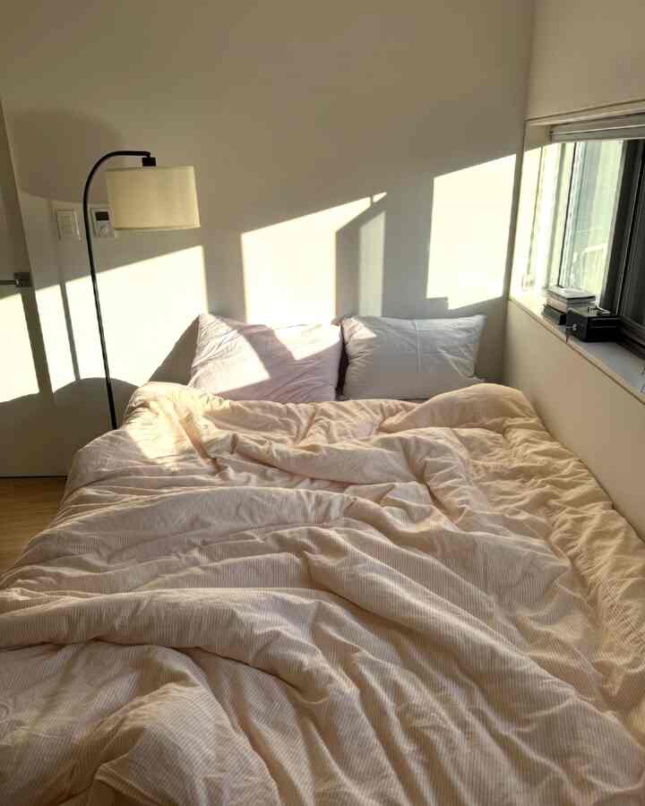 温かみのあるベージュと白のトーンの寝室、窓際に配置された大きなベッドと枕がある雰囲気のあるインテリア