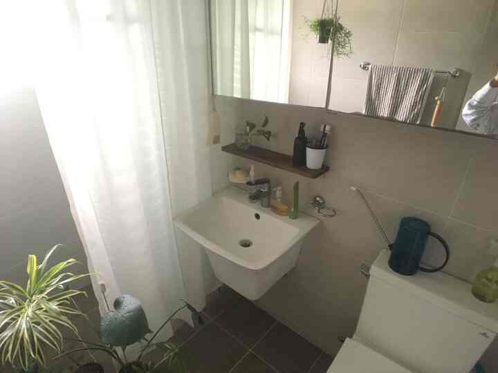 明るいホワイトとナチュラルカラーのバスルーム、壁掛け洗面台と植物の置かれた木製棚、ハンギングプラントが配置された雰囲気のある空間