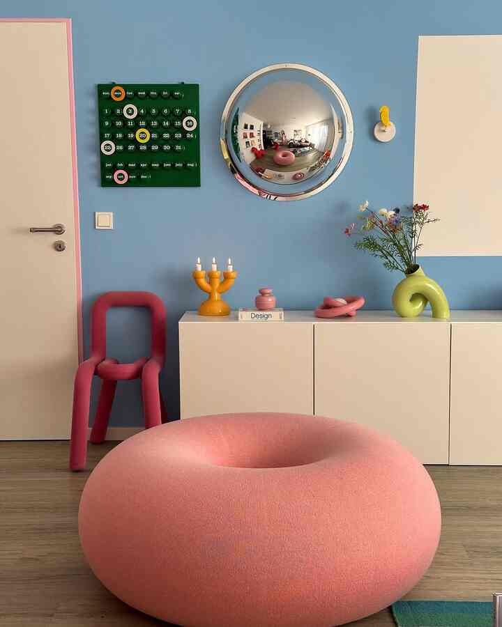Pastel blue wall living room featuring a pink doughnut-shaped pouf and retro mid-century modern furniture with artistic decor