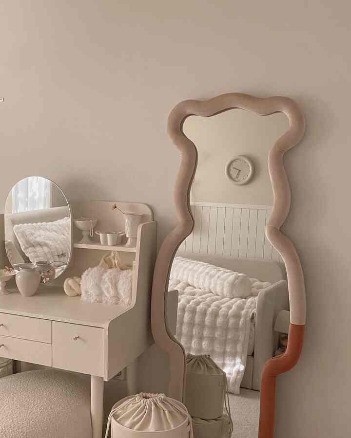 ベージュとクリーム色調の寝室、ユニークな曲線のファブリック全身鏡とクラシックな化粧台が配置された雰囲気のあるインテリア