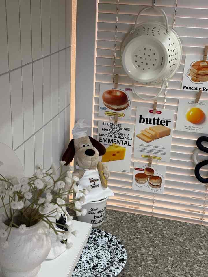 白とグレーのトーンのキッチン、ブラインドが背景にあり、ベーカ－のグロミット人形とキッチン小物が温かみのあるインテリア