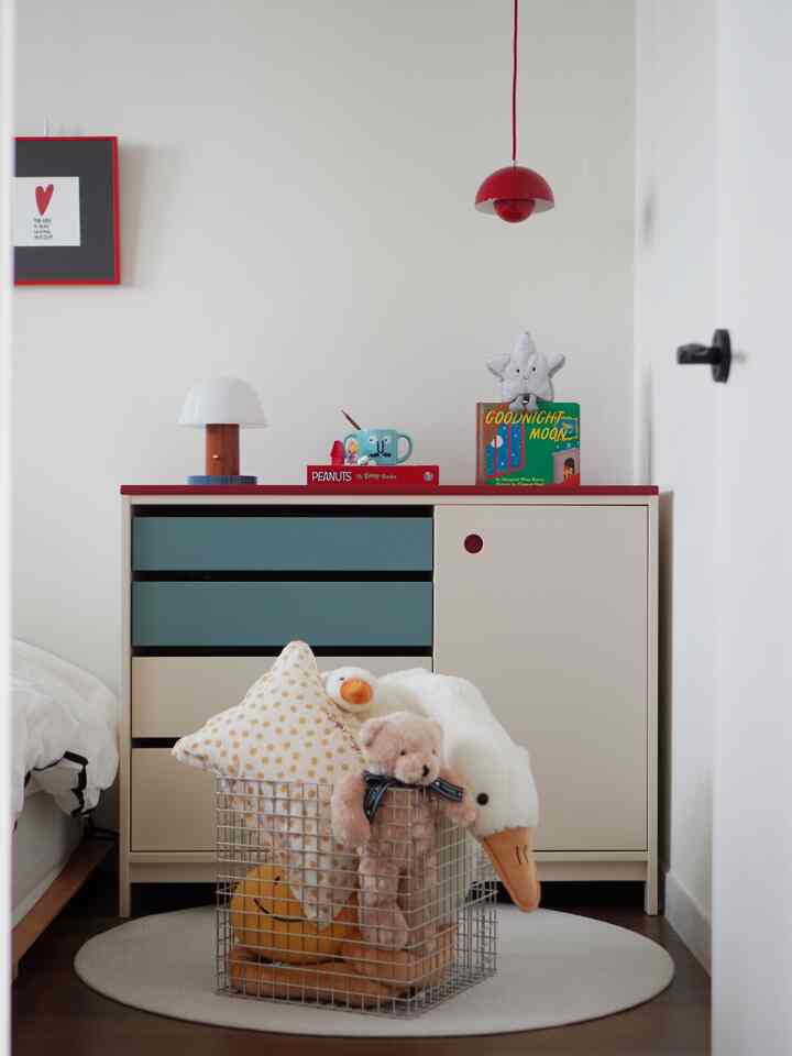 ベージュと青緑のキャビネットがある子供部屋、赤いペンダントライトとおもちゃの入ったバスケットが配置された整った雰囲気のある空間