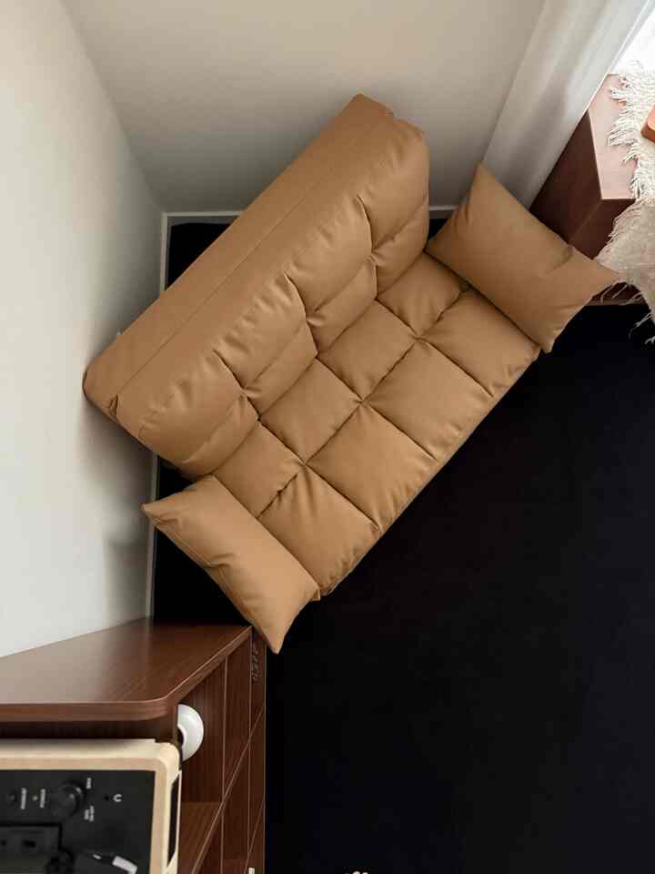 ブラウンとブラックのトーンが調和するコンパクトなリビング、ブラウンのソファベッドと木製収納が置かれた雰囲気のあるインテリア