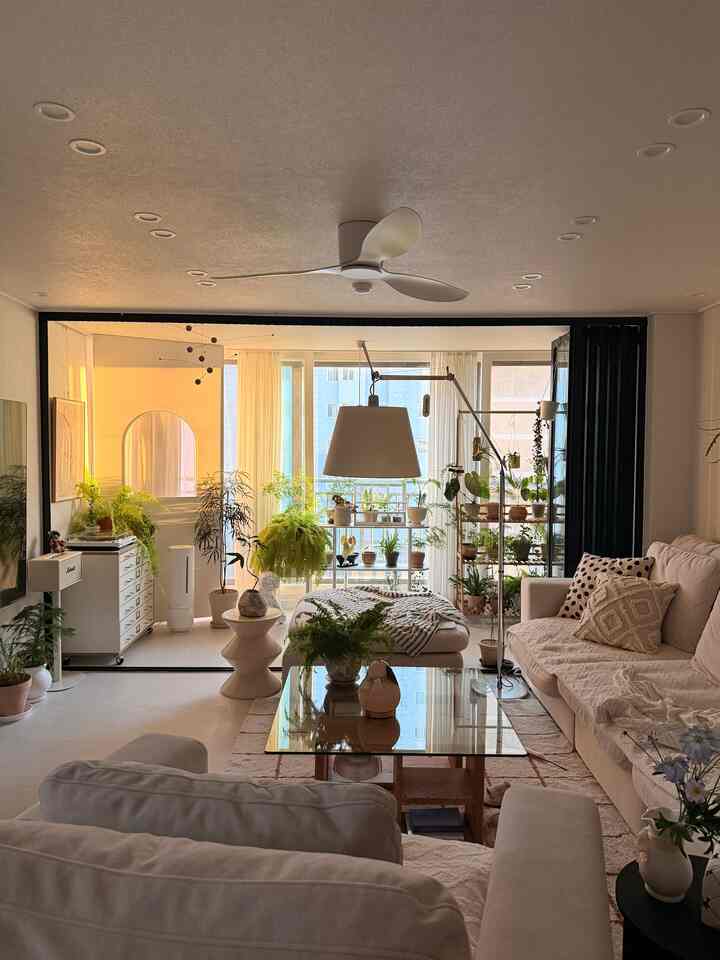 明るいベージュ調のリビング、広いソファとコーヒーテーブル、多数の植物が配置された自然な雰囲気のインテリア