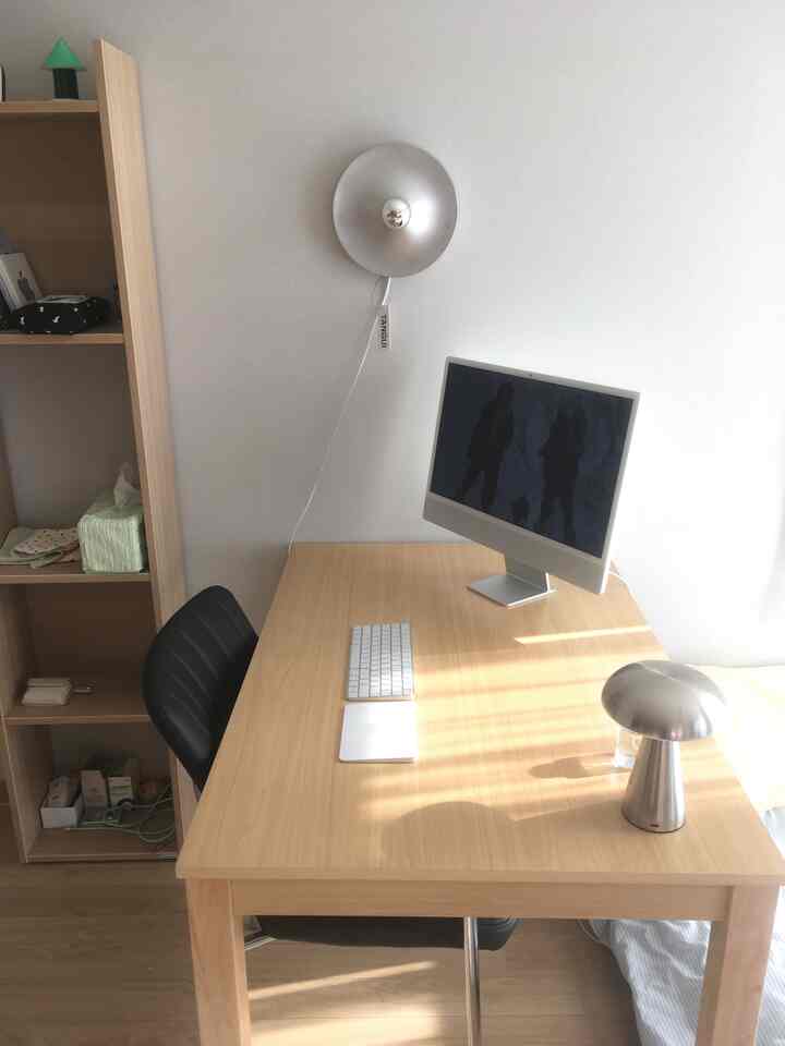 白い壁と天井のあるワンルームのワークスペース、木製の机の上にAppleのiMacとムードランプが配置されたモダンな空間