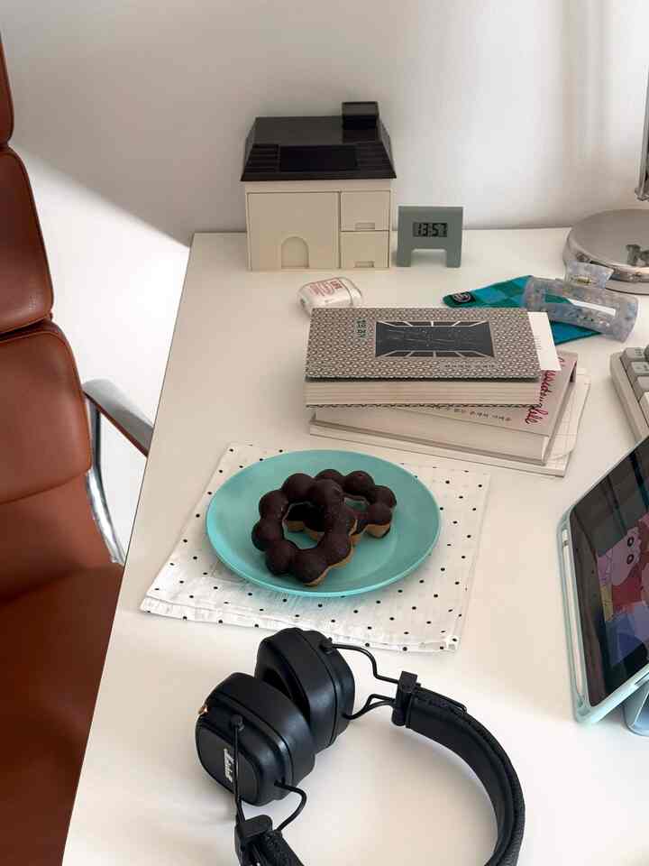 白色のホームオフィス空間、デスク上にヘッドホンとドーナツの皿が配置された、落ち着いた印象の作業スペース
