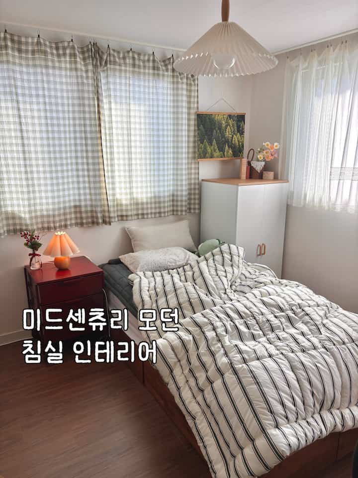 ナチュラルカラーと木目調の寝室、ストライプの寝具とバーガンディのチェストが配置されたミッドセンチュリーモダンなインテリア