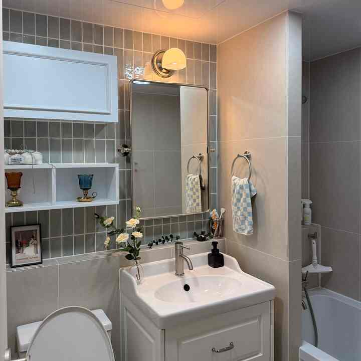 ベージュと白の色調のバスルーム、洗面台と鏡、ブラケットライトとタオルが配置された清潔感のある印象的な空間