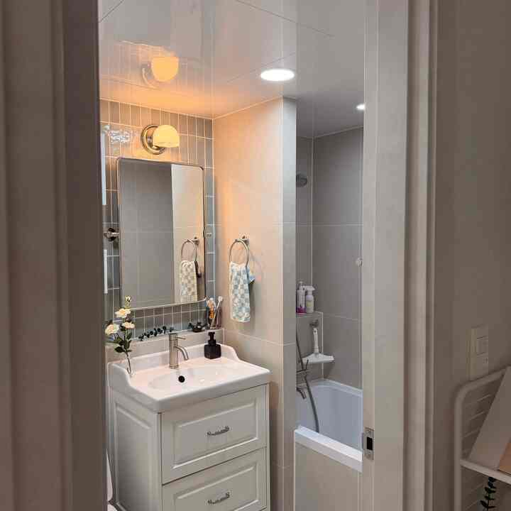 白とベージュのトーンのバスルーム、洗面台と鏡、タオル掛け、浴槽が配置された雰囲気のある空間