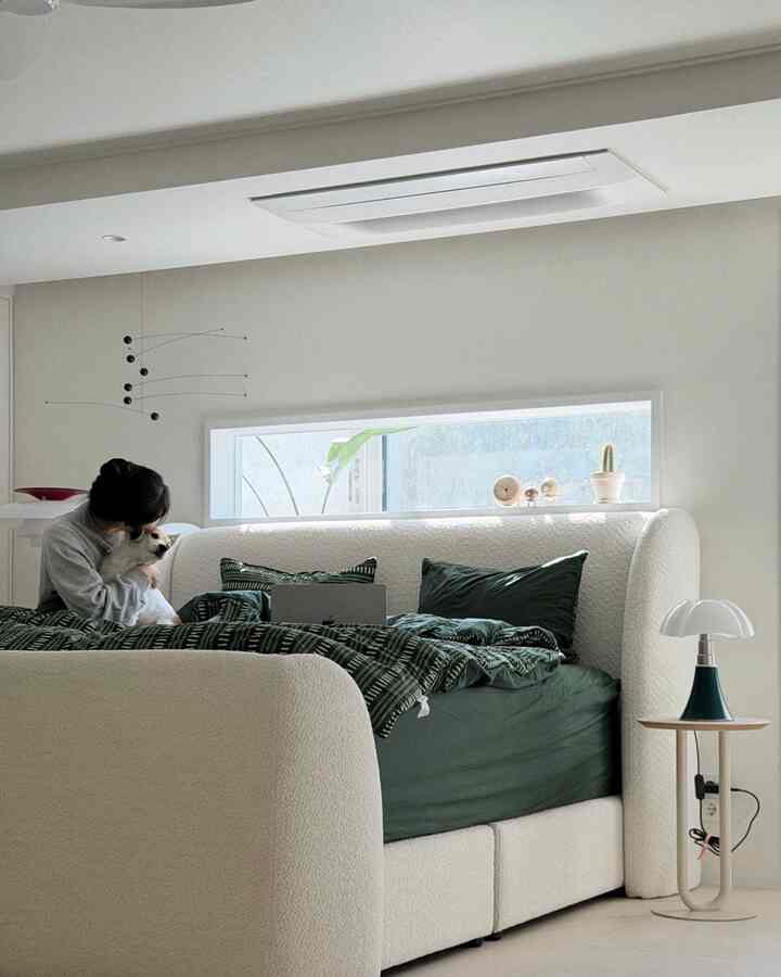 白と緑のトーンの寝室、大きなソファベッドとテーブルランプ、ペットの犬と共にある落ち着いた空間