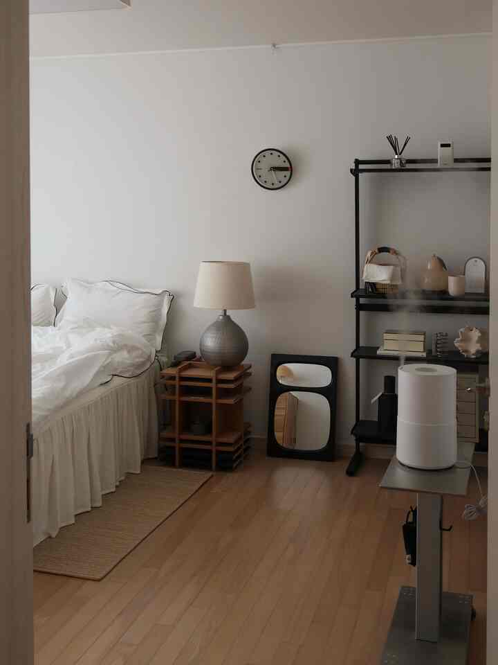 ホワイトとウッドトーンの寝室、ナイトテーブルと照明が配置され、ミニマルで整った雰囲気のあるインテリア