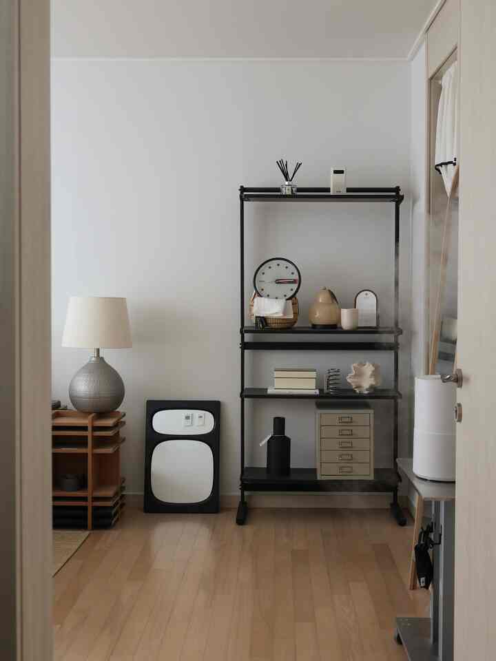 白い壁と木製の床が調和するミニマルでナチュラルな空間、収納棚とフロアランプが配置されたすっきりとした部屋