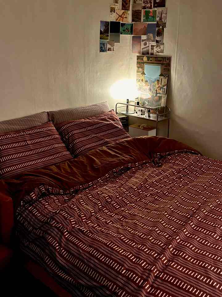 ブラウン系の寝具と枕がある寝室、壁に写真が飾られ、温かい照明が配置された雰囲気のある空間